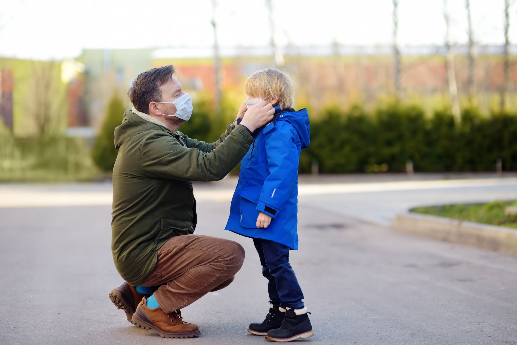man wearing a jacket and a medical mask adjusting his son's medical mask outside