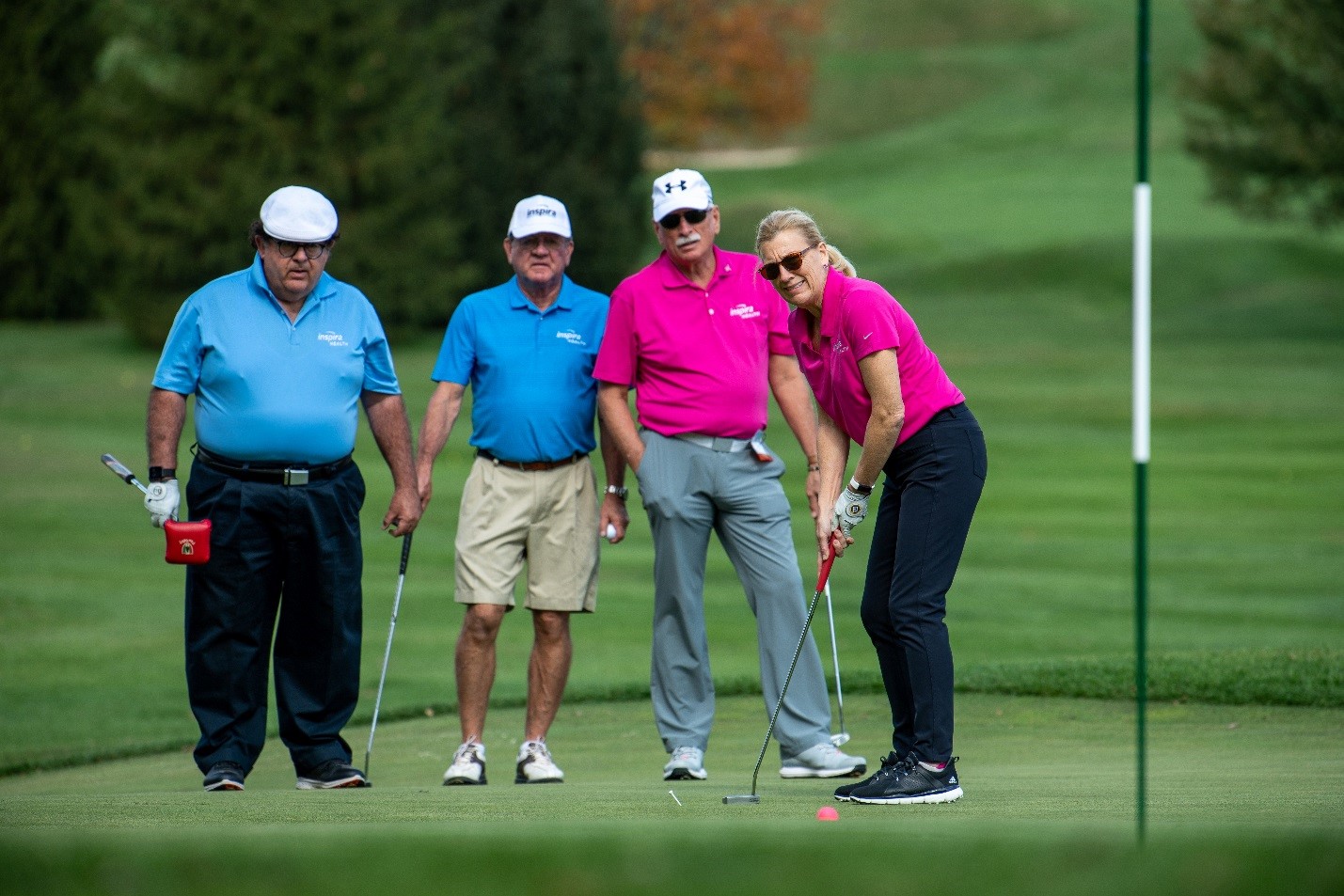amy mansue putting on the green with a group of men behind her