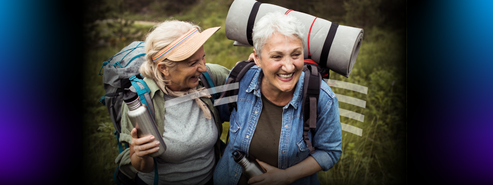two older women laughing and hugging while hiking and carrying reusable water bottles and backpacks